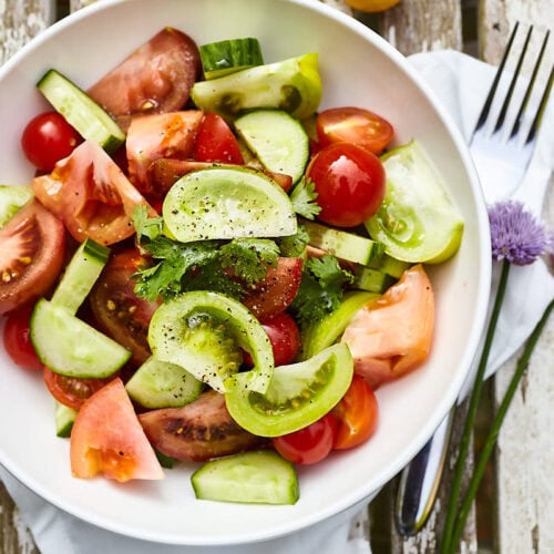 Verse tomatensalade met komkommer en kruiden op houten tafel.