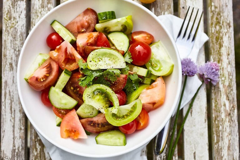 Verse tomatensalade met komkommer en kruiden op houten tafel.
